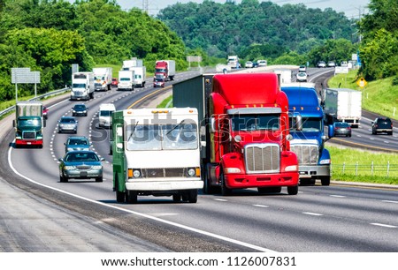 American colors reflect in three trucks leading traffic on an interstate highway. Shot on hot day. Asphalt heat waves cause distortion on vehicles farther from camera, enhancing long telephoto effect.