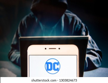 American Comic Book Publisher Company DC Comics Logo Is Seen On An Android Mobile Device With A Figure Of Hacker In The Background.