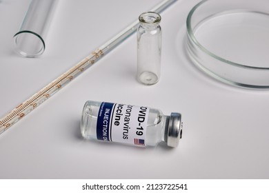 American Covid Vaccine And Chemical Glassware - Labs Photo. Coronavirus Antivirus Solution Inside Glass Bottle. Immunization Shot On Lab Desk. Antiviral Therapy Against Coronavirus And Flu Infection.