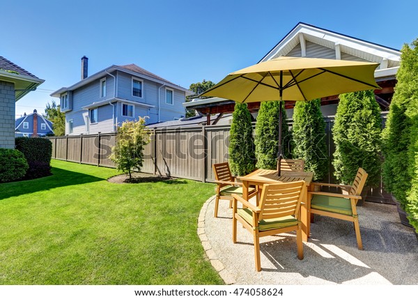 American craftsman house exterior. Small\
Patio area with wooden table set and umbrella. Green thuja trees in\
pots and well kept lawn. Northwest,\
USA