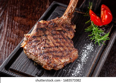 American cuisine. Large juicy grilled steak on a tomahawk bone. Beef steak on a wooden board with rosemary and salt. background image, copy space text - Shutterstock ID 1683573382