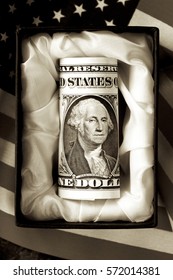 An American Dollar Note In A Casket With The Flag In Sepia Tone.