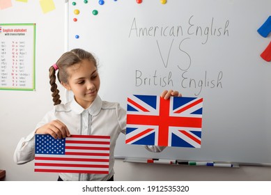 American English VS British English concept. Cheerful schoolgirl with American and British flags in the classroom, learning differences in types of English languages