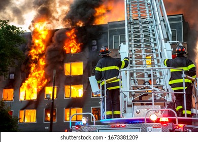 American firefighters on the turntable of a fire department ladder truck at the scene of a major fire that destroyed a large apartment complex under construction