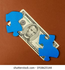 American Five Dollar Bill And Puzzle Pieces On Brown Background. Blue Puzzles With Money. Top View, Flat Lay.