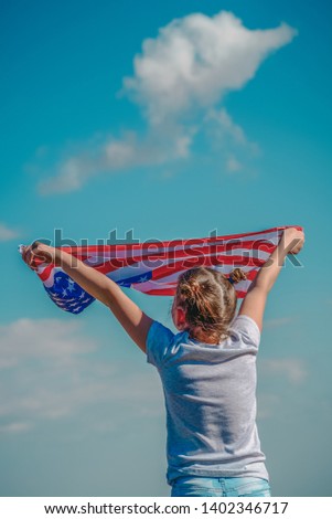 American flag. Back view little patriotic happy girl holding an american flag waving on blue sky background. National 4 july. Memorial day. Retro style.