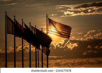 American flag baclkit by sun at cloudy sunset waving in wind left to right with a group of other flags sihouetted  - Shutterstock ID 1514177678