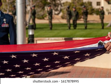 American Flag Being Folded With Soldiers In Background With Rifles Raised During A 21 Gun Salute