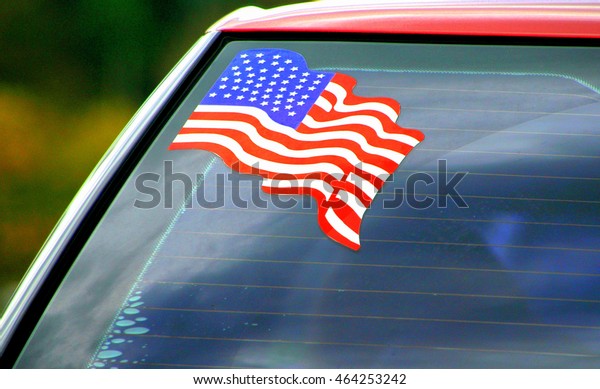 American flag\
decal on a car windshield\
outdoors.