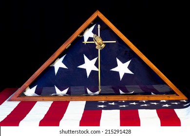 American Flag Encased In Box With Brass Praying Hands Cross In Forefront.  Flag In Background.