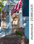 American flag entrance to home decorated for traditional fall holidays, wreath on door, pumpkins on front steps. 