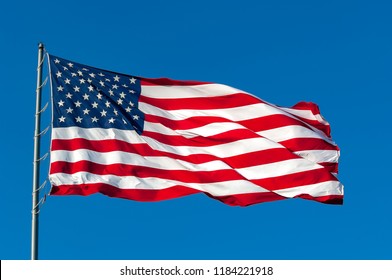 An American flag flying in the breeze against a cloudless bright blue sky.
