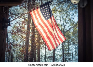 American flag flying on wooden pole on patio of cabin at nature park outside of Houston, Texas, America. Lookup view of waving flag of USA with rustic outdoor wall lamp in natural setting - Powered by Shutterstock