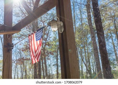 American flag flying on wooden pole on patio of cabin at nature park outside of Houston, Texas, America. Lookup view of waving flag of USA with rustic outdoor wall lamp in natural setting - Powered by Shutterstock