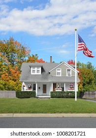 American Flag Front Yard Lawn Suburban Cape Cod Style Home Autumn Day Blue Sky Clouds USA