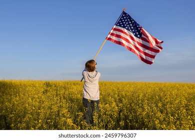 American flag is in hands of woman standing with back among blooming yellow rapeseed field. US Independence Day July 4th. Pride in one's homeland, freedom, patriotism, democracy. Travel around country - Powered by Shutterstock