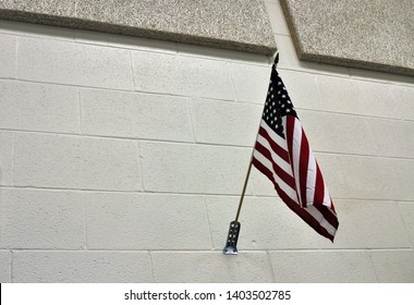 An American Flag hanging in a classroom against a Cream colored Concrete Wall