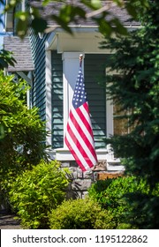 An American Flag Hanging In The Front Of A Home In A Neighborhood. Vertical Photo And Selective Focus On The Flag