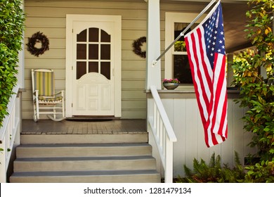 American flag hanging on the front porch of a suburban house.
