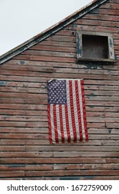 American Flag Hanging On Rustic Wood Sided House With Peeling Paint