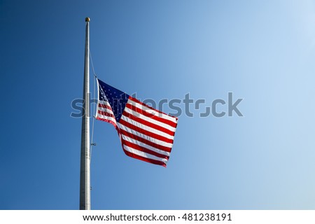 American flag lowered to half mast in bright blue sky