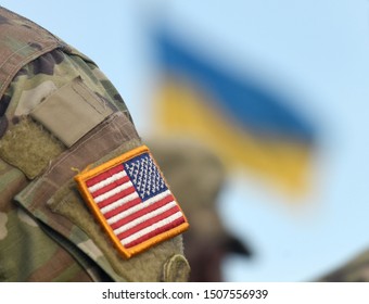 American Flag On Soldiers Arm And Flag Of The Ukraine At Background. US Military Help To Ukraine.