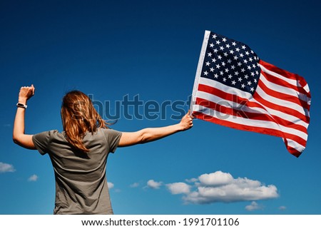 American flag outdoors. Woman holds usa national flag against blue cloudy sky. 4th July Independence Day