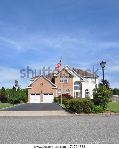 American Flag pole front yard lawn of Suburban\
McMansion style brick home Landscaped sunny residential\
neighborhood USA blue sky\
clouds
