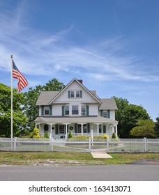 American Flag Pole Large Suburban Home With White Picket Fence Sunny Blue Sky Clouds USA Residential Neighborhood