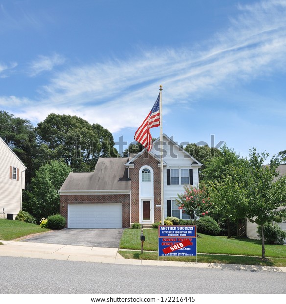 American Flag pole real\
estate sold (Another success let us help you buy sell your next\
home) sign suburban mcmansion style home residential neighborhood\
usa blue sky clouds