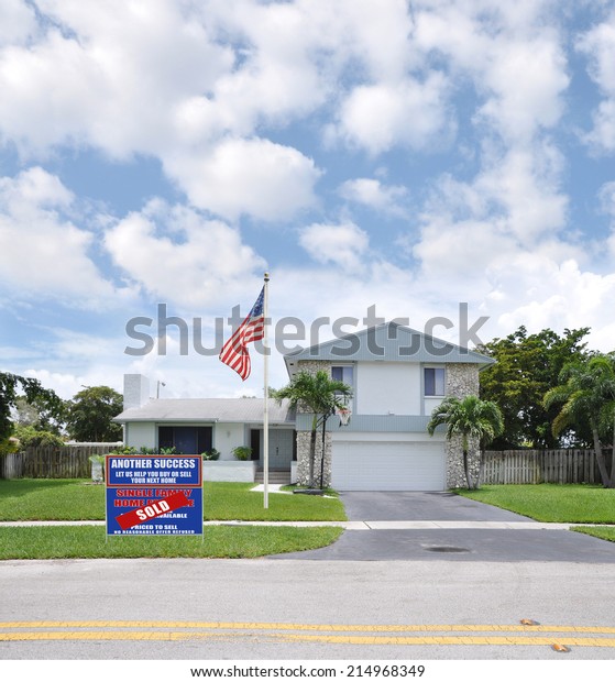 American Flag pole Sold (Another Success let us\
help you buy sell your next home) Real Estate Sign on front yard of\
Suburban Back Split style home residential neighborhood USA blue\
sky clouds