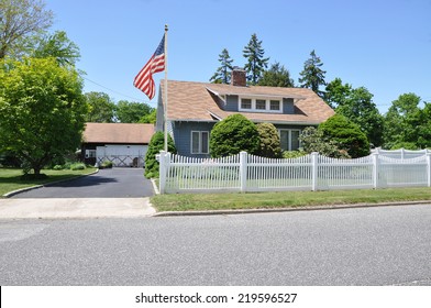 American Flag Pole Suburban cape cod style home with white picket fence residential neighborhood clear blue sky USA