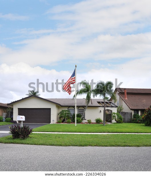 American flag pole Suburban Ranch style\
home residential neighborhood street blue sky clouds\
