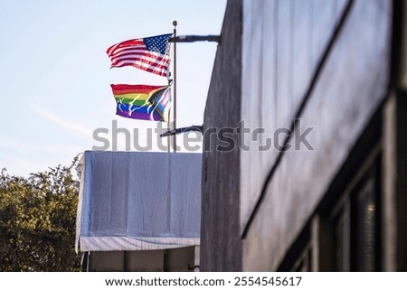American flag and Pride flag flying together on a sunny day, symbolizing unity and diversity.