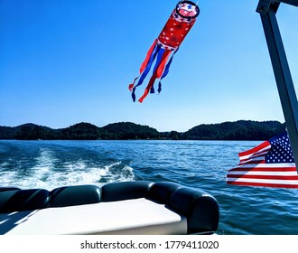 American Flag With Red, White And Blue Decorations Streaming Off The Back Of A Boat On A Tennessee River. Wake From The Boat Motor And Mountains In The Background.