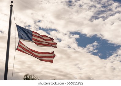 American flag torn down the middle twisting in the wind on a cloudy sky