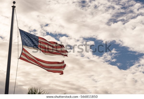 American flag torn down the middle waving in the wind\
on a cloudy sky