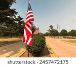 American Flag Waves at the entrance to a cemetery. Park-like setting in the background of view. Located at the entrance to Oak Ridge Cemetery in Springfield, Illinois, USA.