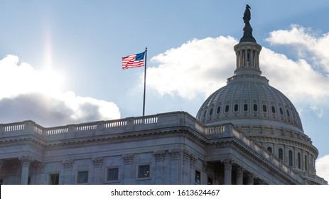 American flag waving atop of United States Capitol Building as the sun shines bright in the background. 