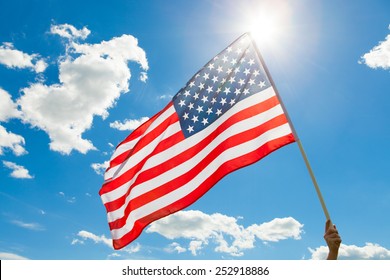 American Flag Waving In Blue Sky With Sun Behind It