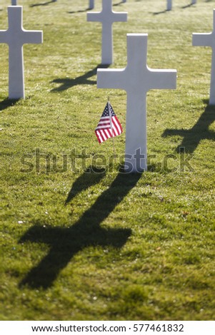 American flag waving next to a cross at the American Cemetery and Memorial near Luxembourg in Europe