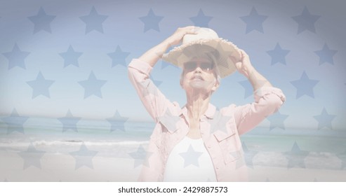 American flag waving over caucasian senior woman wearing a hat at the beach. american independence patriotic holiday concept - Powered by Shutterstock