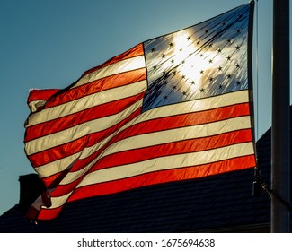 The American flag waving in the wind with the sun shining thru the stars, almost creating a cross pattern on the flag. 