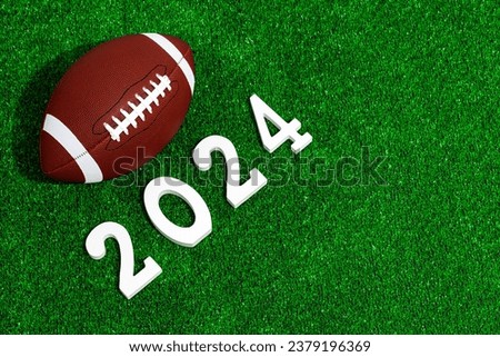 American football ball next to 2024 number whose figures are made of white painted wood isolated over green grass seen from above.