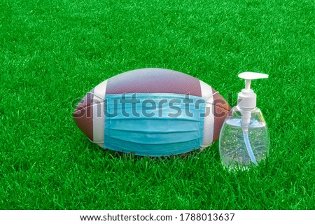 An American Football with a facemask and hand sanitizer on field with green grass. Concept Football during pandemic