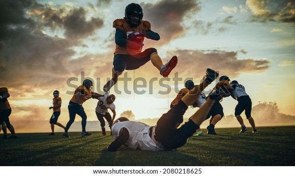 American\
Football Field Start of Offensive Play with a Snap Pass: Successful\
Player Jumping Over Defense Running to Score Touchdown Points.\
Professional Athletes Compete Fight for\
Victory