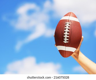 American Football in Hand over Blue Sky - Powered by Shutterstock