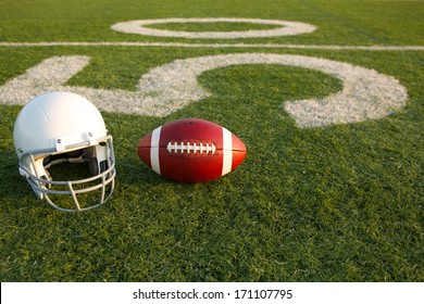 American Football And Helmet On The Field With The Fifty Yard Line In The Background