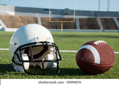 American Football And Helmet On Field With Goal Post In Background.