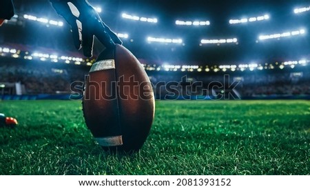 American Football Kickoff Game Start. Close-up Shot of an American Ball Standing on a Stadium Field Held by Professional Player. Preparation for Championship Game.